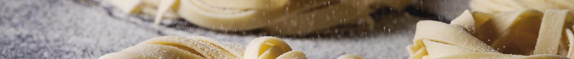 Variety of italian homemade raw uncooked pasta spaghetti and tagliatelle with sprinkling semolina flour over dark plank texture wooden table. Dark rustic style